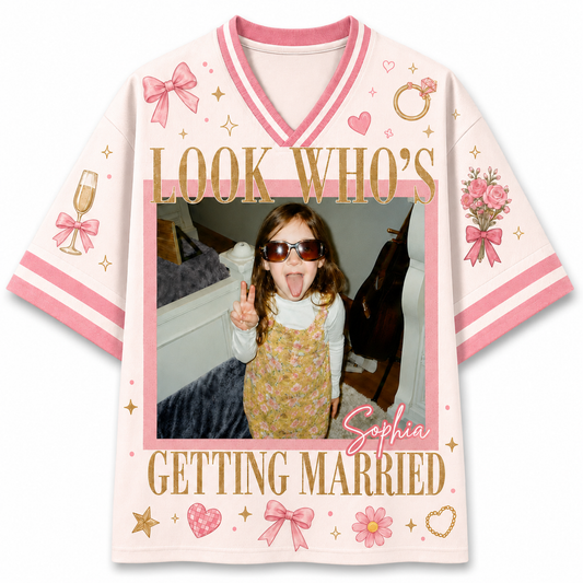A custom short-sleeve V-neck t-shirt with pink and white stripes, featuring a customizable photo frame in the center with the text 'LOOK WHO'S Sophia GETTING MARRIED' in gold, decorated with pink bows, hearts, and flowers.