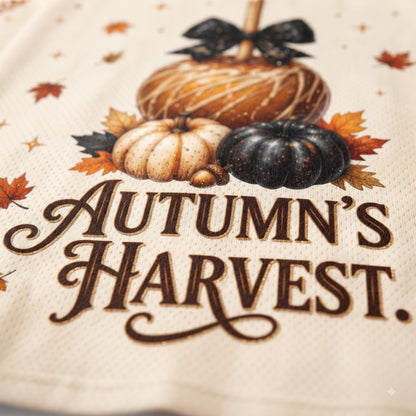 Close-up of a cream-colored woven textile featuring an autumn harvest design with pumpkins, maple leaves, and the words “Autumn’s Harvest.”.