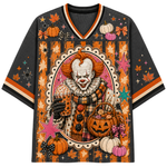 A short-sleeve V-neck t-shirt featuring a detailed Halloween graphic of a clown holding a mug and a pumpkin basket, surrounded by pumpkins, autumn leaves, stars, and stripes in orange, black, pink, and white.
