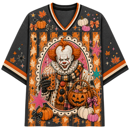 A short-sleeve V-neck t-shirt featuring a detailed Halloween graphic of a clown holding a mug and a pumpkin basket, surrounded by pumpkins, autumn leaves, stars, and stripes in orange, black, pink, and white.