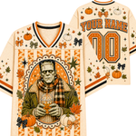 A Halloween-themed football jersey shown from the front and back on a plain white background. The cream-colored jersey features orange and black striped trim, autumn leaves, pumpkins, stars, and bows, with a large graphic of Frankenstein's monster holding a pumpkin on the front.