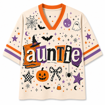 A short-sleeve V-neck t-shirt with a cream base and a colorful Halloween graphic print. The design features the word 'auntie' in a stylized font, surrounded by spiderwebs, bats, a jack-o'-lantern, stars, and other spooky motifs in orange, purple, black, and white.
