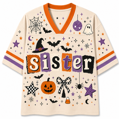 A short-sleeve V-neck t-shirt with a cream base and a colorful Halloween graphic print. The design features the word 'Sister' in block letters, surrounded by spiderwebs, bats, a jack-o'-lantern, a witch hat, a spider, stars, and other spooky motifs.