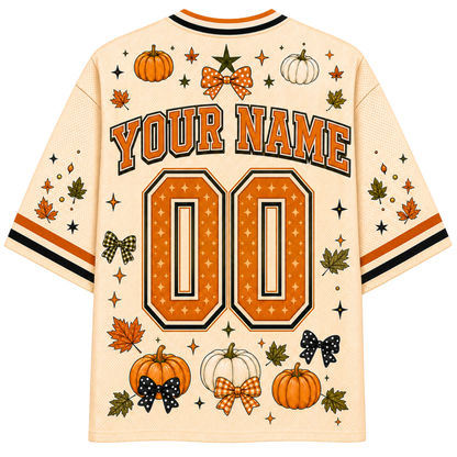 A cream-colored mesh baseball-style jersey shown from the back, featuring customizable orange and black text reading 'YOUR NAME' and '00', surrounded by autumn-themed graphics including pumpkins, stars, leaves, and bows.