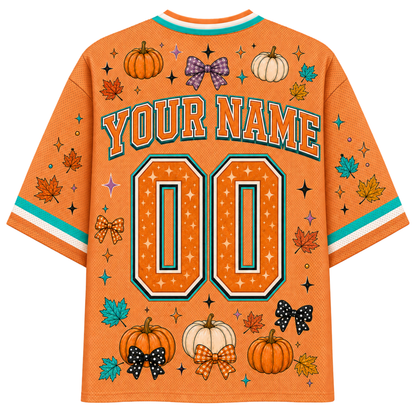 An orange mesh baseball-style jersey shown from the back, featuring a customizable design with 'YOUR NAME' and '00' in large outlined numbers. The shirt is decorated with autumn motifs including pumpkins, maple leaves, bows, stars, and teal and white striped accents on the collar and sleeves.