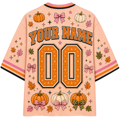 A peach-colored customizable baseball-style jersey shown from the back, featuring orange and black 'YOUR NAME' lettering above large '00' numbers. The design includes orange and white pumpkins, pink bow motifs, autumn leaves, and small stars, with striped collar and sleeve cuffs.