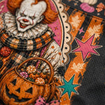 Close-up of a Halloween-themed graphic print featuring a clown, a jack-o'-lantern basket filled with pumpkins, and orange stars on a dark textured background.