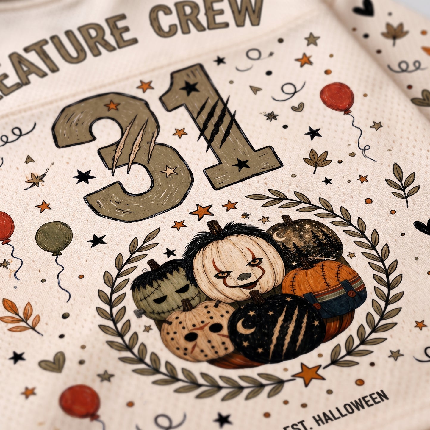 Close-up of a white Halloween-themed printed garment or fabric featuring the number 31, a wreath with pumpkins, stars, leaves, and partial text reading 'Creature Crew' and 'Halloween'.