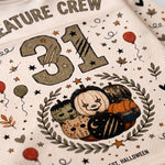 Close-up of a white Halloween-themed printed garment or fabric featuring the number 31, a wreath with pumpkins, stars, leaves, and partial text reading 'Creature Crew' and 'Halloween'.