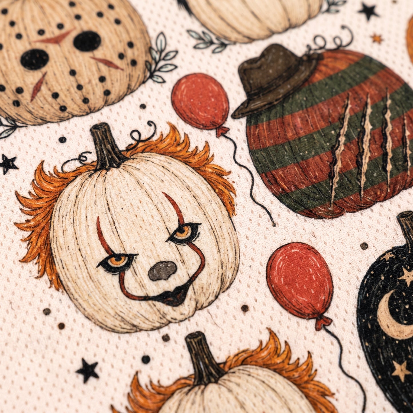 Close-up of a Halloween-themed fabric print featuring clown pumpkins, striped pumpkins, red balloons, stars, and dots on a light beige background.