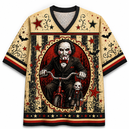 A short-sleeve V-neck t-shirt featuring a detailed graphic print of Leatherface on a red tricycle with Billy the Puppet in front, set against a distressed beige, black, and red circus-style background.