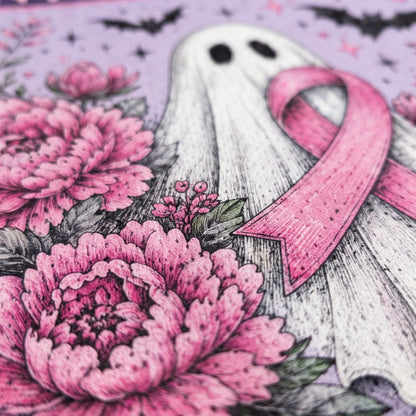 A close-up of a printed design featuring a white ghost with black eyes and a pink ribbon, surrounded by large pink flowers and small black bats on a lavender background.