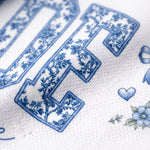Close-up of a white textured fabric with blue floral decorative lettering and small blue floral motifs.