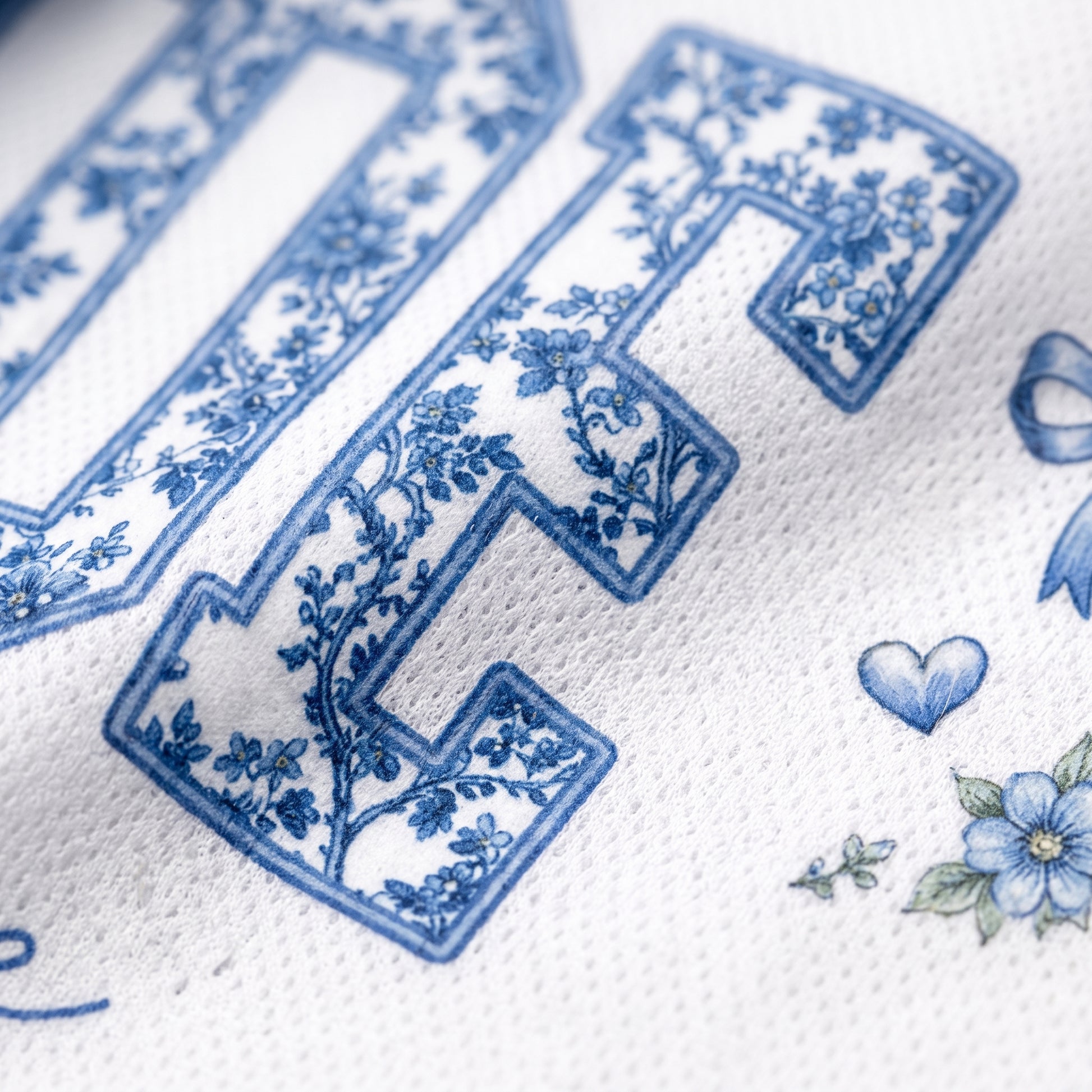Close-up of a white textured fabric with blue floral decorative lettering and small blue floral motifs.