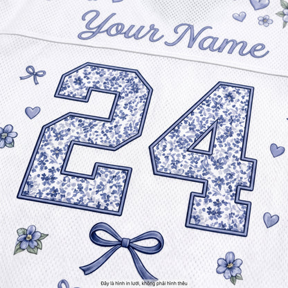 Close-up of a white personalized sports jersey fabric with blue floral patterned number 24, blue script 'Your Name' at the top, small blue flowers and hearts, and a blue bow graphic.