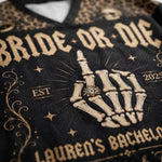 Close-up of a black mesh sports jersey with a beige skeleton hand graphic wearing a ring, surrounded by gothic-style text reading 'BRIDE OR DIE' and 'LAUREN'S BACHELOR'.