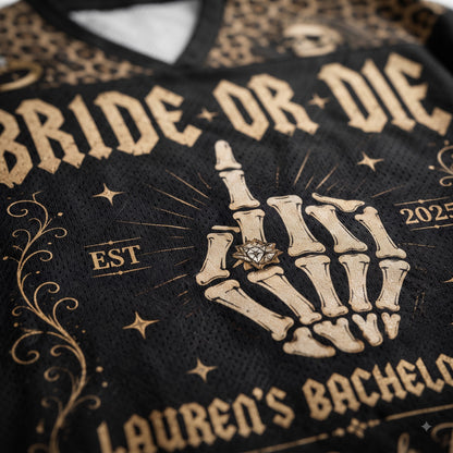 Close-up of a black mesh sports jersey with a beige skeleton hand graphic wearing a ring, surrounded by gothic-style text reading 'BRIDE OR DIE' and 'LAUREN'S BACHELOR'.