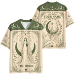 A short-sleeve V-neck t-shirt shown from both front and back, featuring a celestial tarot-style design in dark green on a warm cream base. The front displays 'THE BRIDE' with an illustration of a woman in a gown standing on a crescent moon.