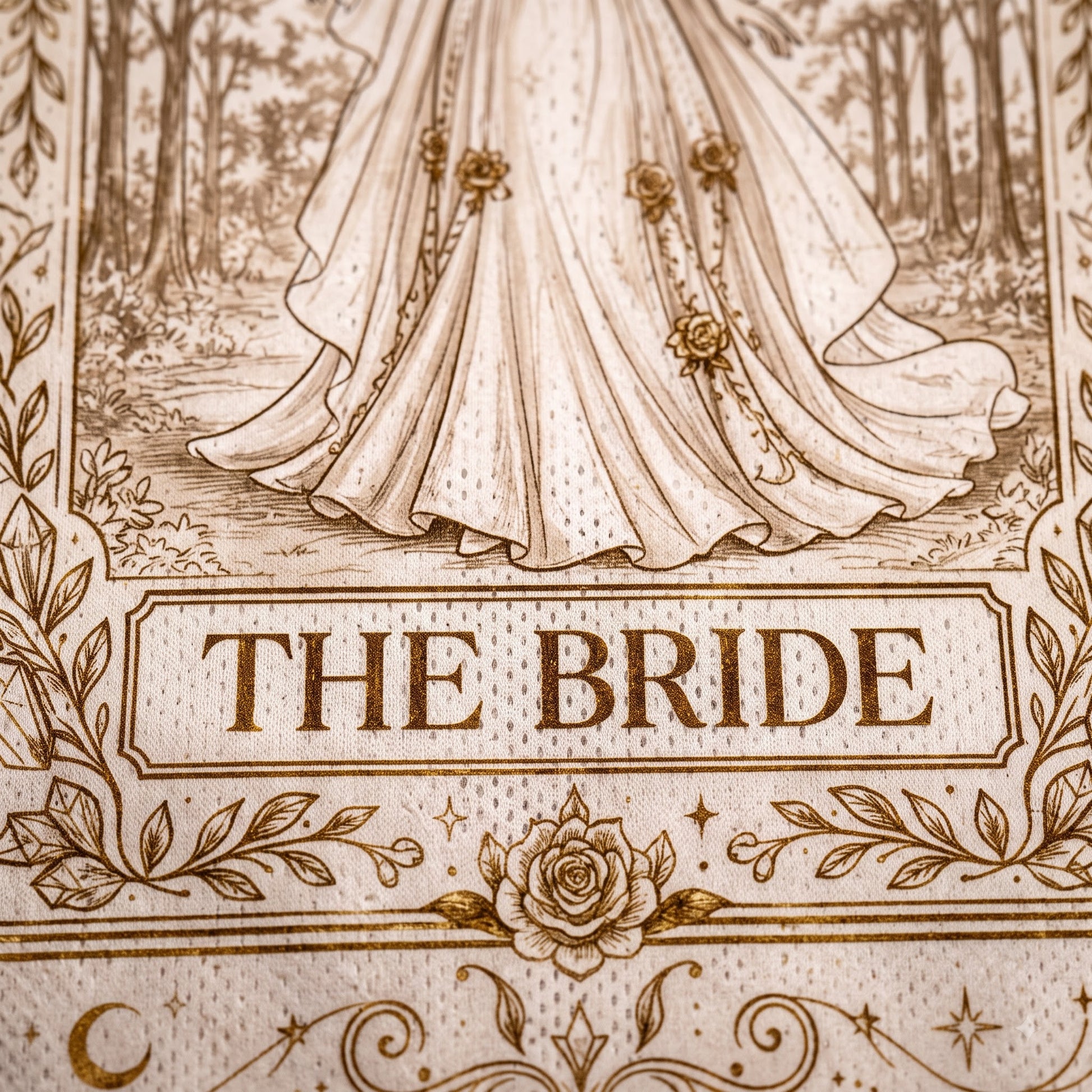 A close-up of a printed textile or fabric design featuring an illustration of a bride's flowing gown in a forest scene, with the words 'THE BRIDE' in a decorative panel and floral border details.