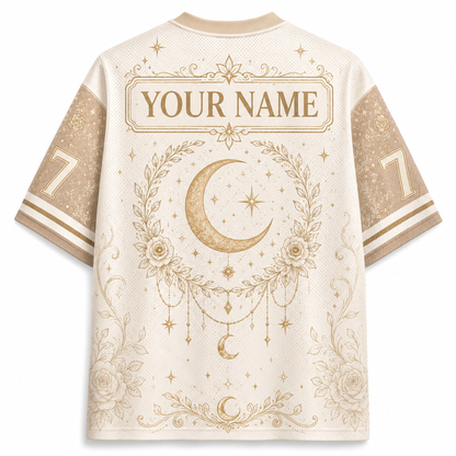 Back view of a short-sleeve athletic jersey in cream with gold celestial graphics, including a large crescent moon, stars, floral wreath, and a customizable name patch reading 'YOUR NAME'.