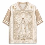 A short-sleeve V-neck jersey-style shirt in warm cream and beige with a large central tarot-card-inspired illustration reading "THE BRIDE," plus moon, star, and floral decorative motifs on the sleeves and body.