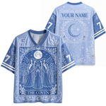 Front and back views of a light blue V-neck jersey with a detailed blue and white celestial 'The Coven' tarot card design, featuring a customizable name patch on the back.