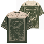A dark green and beige V-neck t-shirt with celestial and tarot card themed graphics, shown in both front and back views. The front features 'THE COVEN' text and moon phases, while the back displays 'YOUR NAME' in a decorative frame.