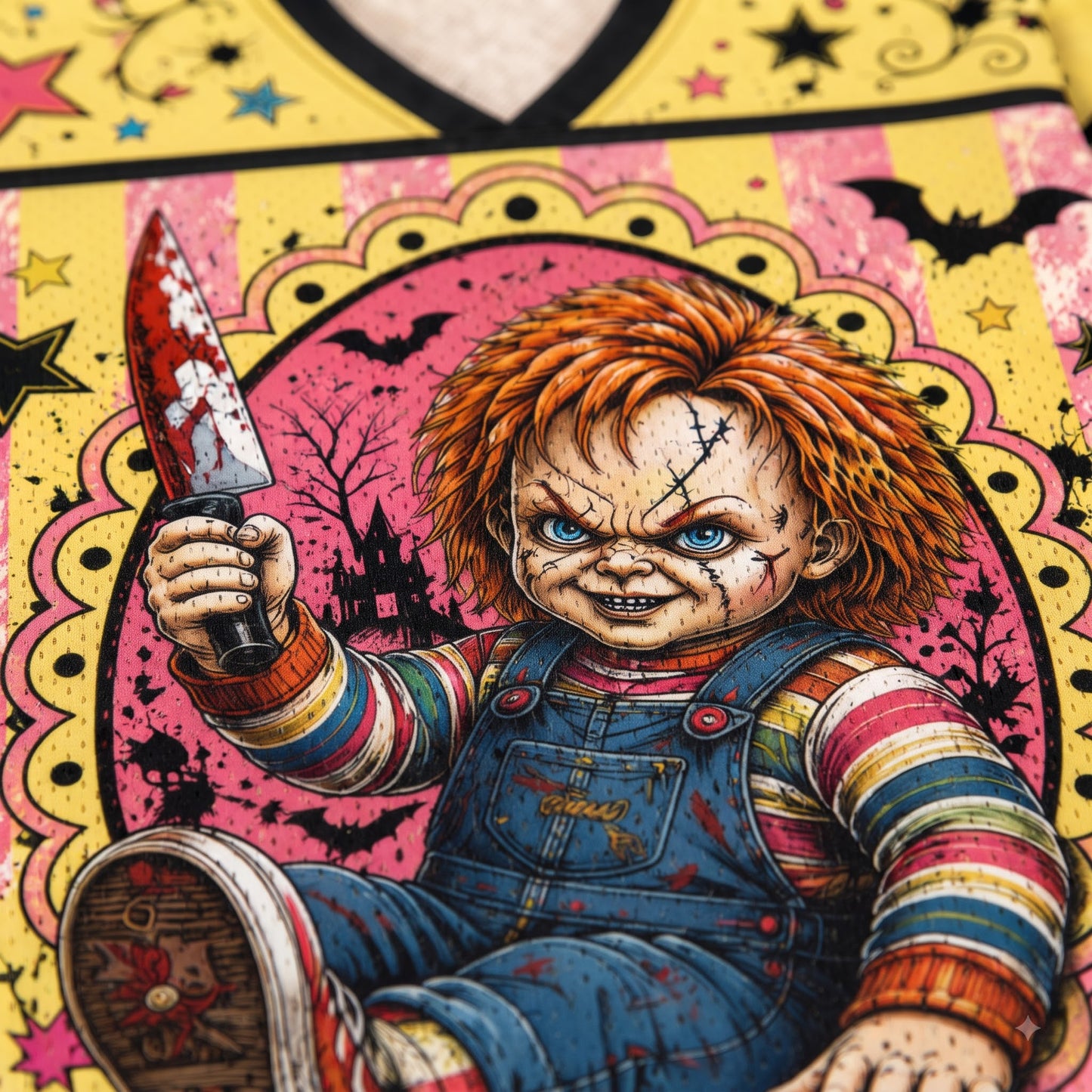 A close-up of a graphic print featuring Chucky holding a bloody knife, set against a pink and yellow Halloween-themed background with bats, stars, and a haunted house.