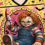 A close-up of a graphic print featuring Chucky holding a bloody knife, set against a pink and yellow Halloween-themed background with bats, stars, and a haunted house.