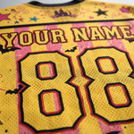 Close-up of a yellow mesh sports jersey with pink and black striped accents, featuring customizable 'YOUR NAME' text and the number '88' in large outlined numerals. Bats, stars, and castle motifs decorate the design.