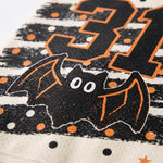 Close-up of a Halloween-themed graphic print featuring a black bat with orange outlines, white polka dots, and a large black and orange number 31 on a textured light background.