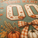 Close-up of a personalized sports jersey fabric featuring autumn-themed graphics, including the number 00 in a decorative border with pumpkins and flowers, a gingham bow, wheat stalks, and a white pumpkin on a muted green mesh background.