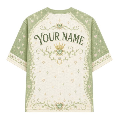 A short-sleeve t-shirt with a custom print area on the back, featuring a sage green and cream color scheme with a crown, ring, and floral scroll designs, and the text 'YOUR NAME'.