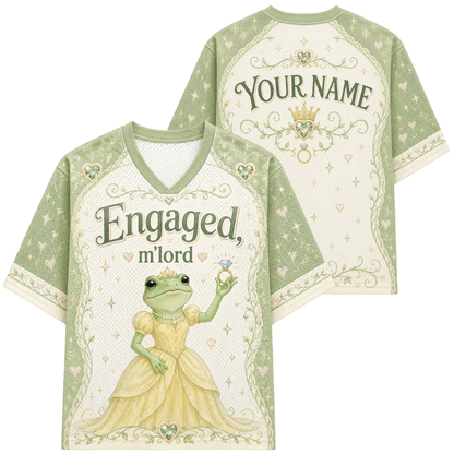 A short-sleeve V-neck t-shirt shown from both front and back. The shirt features a light sage green and cream color scheme with a central illustration of a princess frog holding a diamond ring.