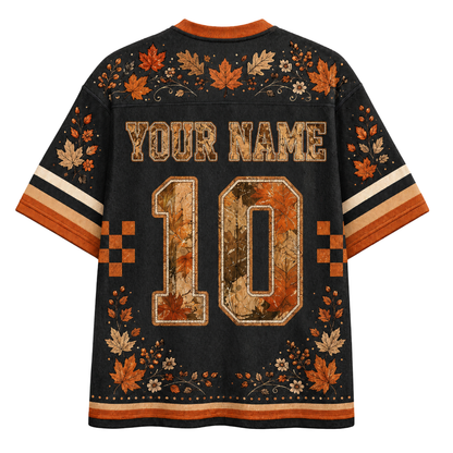 Back view of a customizable black short-sleeve jersey with orange and beige autumn-themed leaf patterns, 'YOUR NAME' text, and the number '10' on a solid white background.