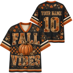 A black short-sleeve V-neck jersey-style shirt shown from the front and back, decorated with autumn fall leaves, a pumpkin graphic, checkered orange accents, and distressed text reading 'FALL VIBES' on the front. The back shows 'YOUR NAME' and a large number '10'.