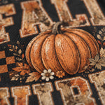 Close-up of a black mesh fabric with a fall harvest graphic featuring a textured orange pumpkin, autumn leaves, small white and orange flowers, and distressed beige letters on a black background.
