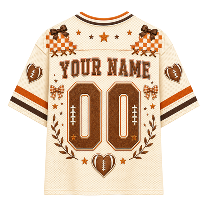 Customizable football jersey back view with 'YOUR NAME' and number '00' in brown, decorated with stars, checkered patches, heart and football motifs on an off-white mesh fabric.