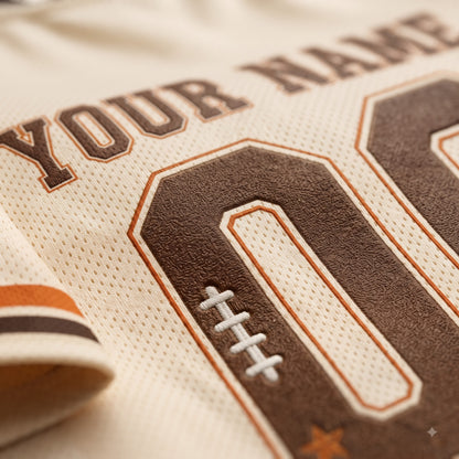 Close-up of a custom sports jersey featuring a cream-colored mesh fabric with brown and orange athletic lettering and numbers, including a football patch detail.