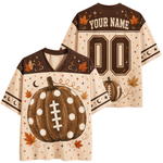 A custom football-style jersey shown from both front and back on a plain white background. The shirt has a cream base with brown shoulder panels, a large brown polka-dotted pumpkin with white laces on the front, autumn leaves, stars, moons, and decorative dots.