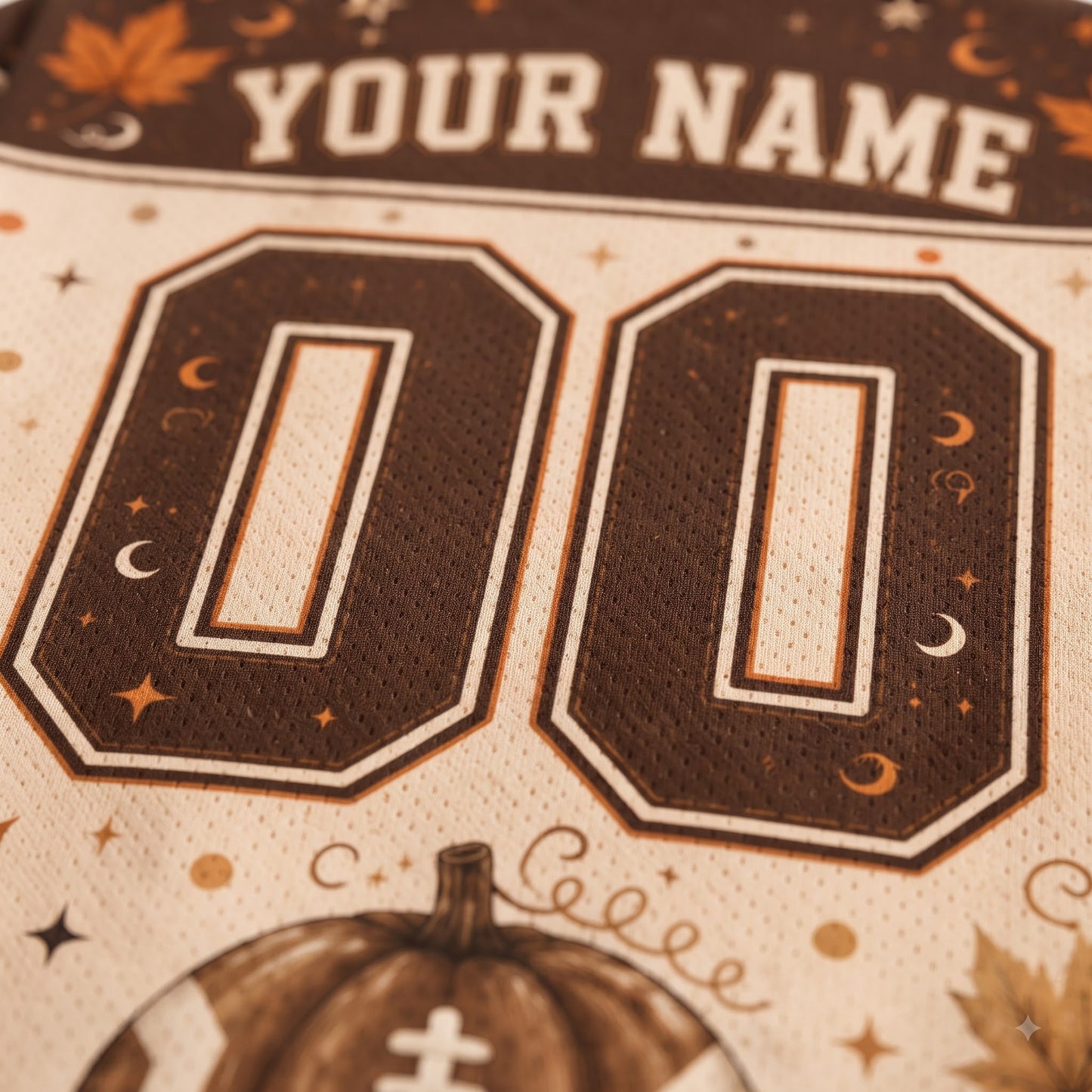 Close-up of a customizable sports jersey fabric with 'YOUR NAME' at the top, large '00' numbers, and a pumpkin graphic at the bottom.