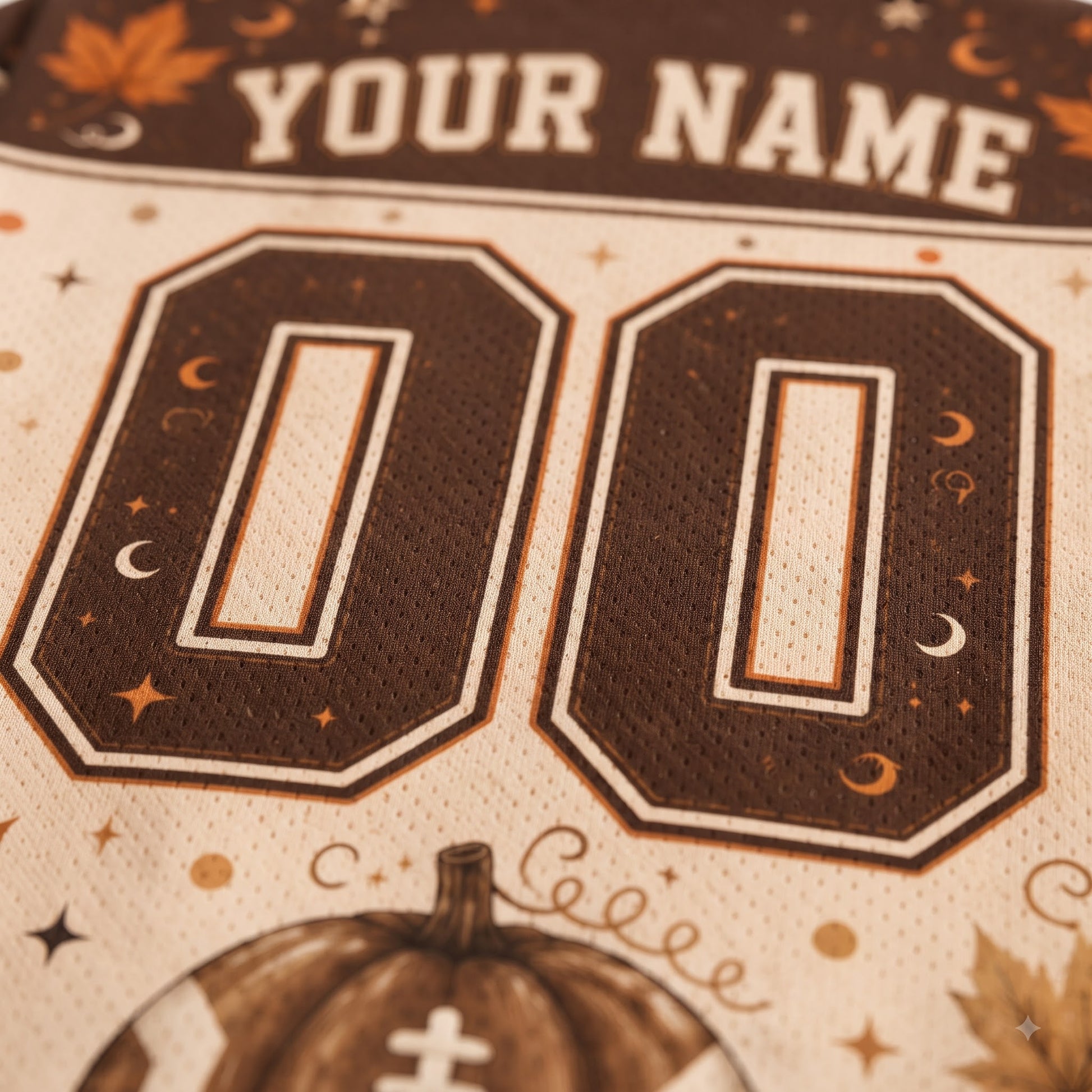 Close-up of a customizable sports jersey fabric with 'YOUR NAME' at the top, large '00' numbers, and a pumpkin graphic at the bottom.