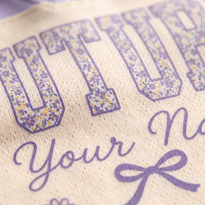 Close-up of a cream-colored knit fabric with purple text reading 'FUTURE Your Na.