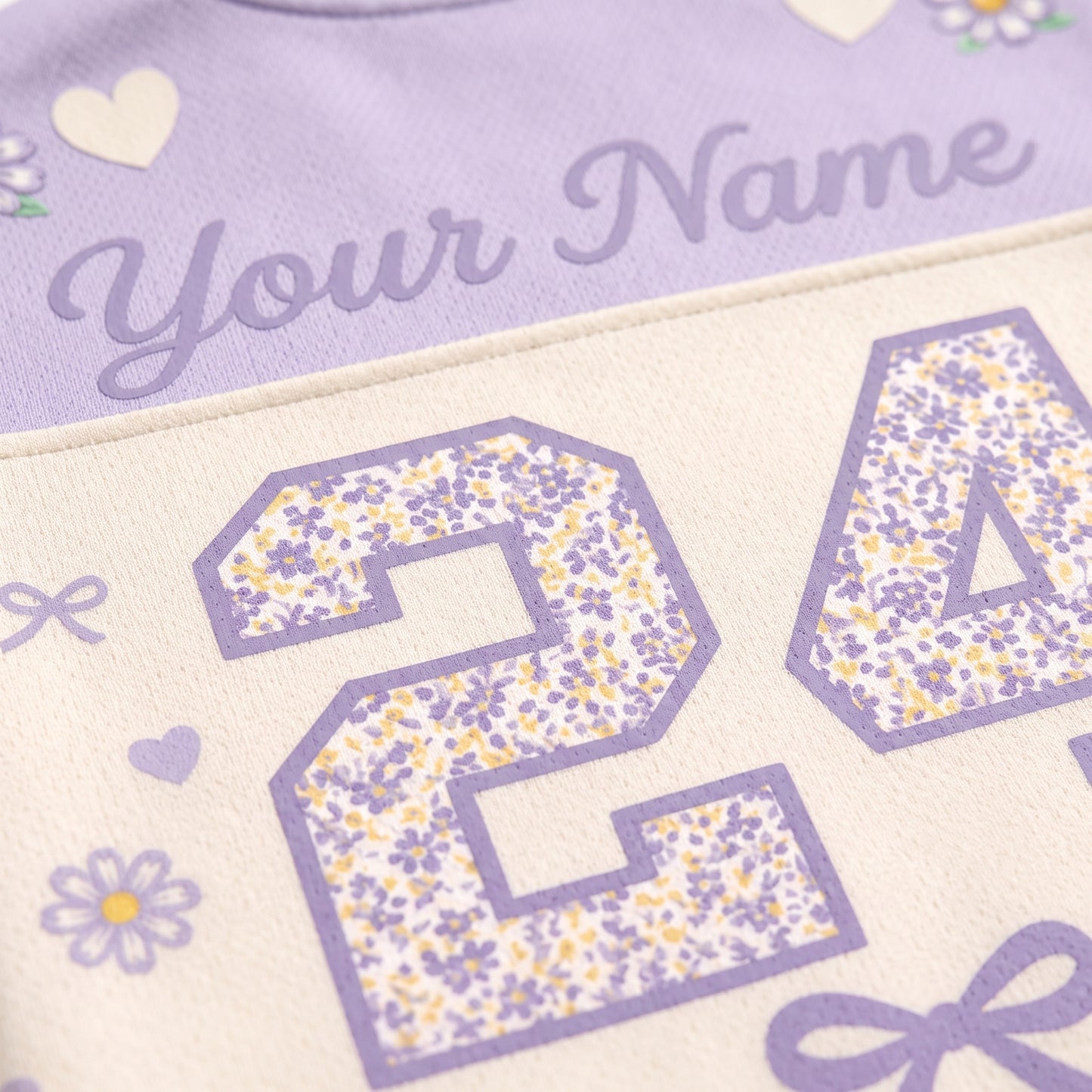 Close-up of a personalized sports jersey fabric with lavender purple text reading 'Your Name' and floral-patterned numbers on a cream background.