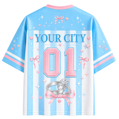 A custom short-sleeve jersey shown from the back, featuring a light blue and white vertical stripe pattern. The back is decorated with pink and blue details, including the text 'YOUR CITY', the number '01' in pink, and an illustration of two engagement rings tied with a pink bow.