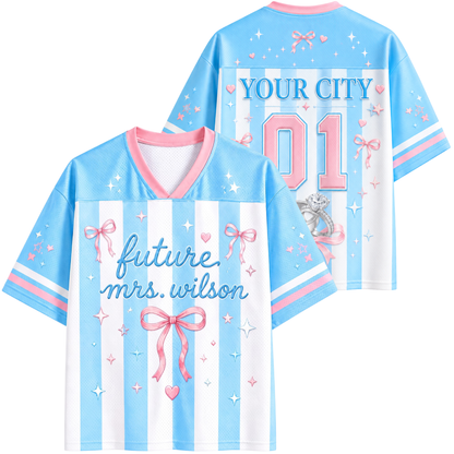 Customizable short-sleeve V-neck sports jersey shown from both front and back. The jersey features light blue and white vertical stripes, pink and blue lettering, and pink bows with star accents.