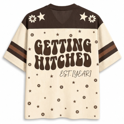 A retro-style short-sleeve t-shirt with a cream and dark brown color-blocked design. The back features the text 'GETTING HITCHED EST.