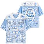 A light blue and white short-sleeve V-neck t-shirt shown from both front and back, decorated with blue wedding-themed illustrations and customizable text including 'future Mrs. Miller', 'Oliver + Megan', and 'it's giving wife'.