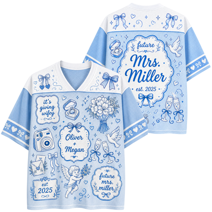 A light blue and white short-sleeve V-neck t-shirt shown from both front and back, decorated with blue wedding-themed illustrations and customizable text including 'future Mrs. Miller', 'Oliver + Megan', and 'it's giving wife'.