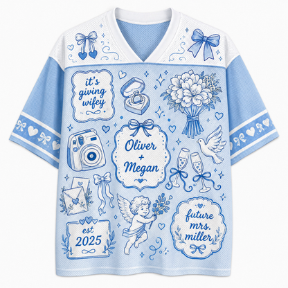 A light blue and white short-sleeve V-neck t-shirt with blue line-art illustrations and text celebrating a wedding, including 'it's giving wifey', 'Oliver + Megan', 'future Mrs. Miller', and 'est.